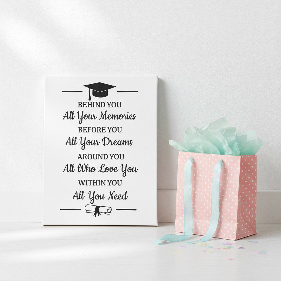 Graduation quote canvas print leaning against white wall beside pink polka dot gift bag with mint tissue paper, thoughtful graduation gift idea