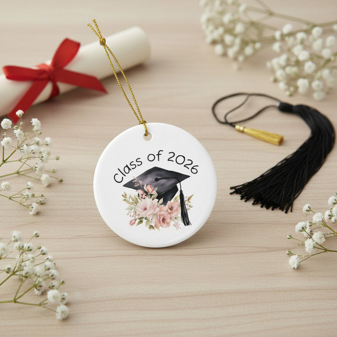 Class of 2026 floral ceramic ornament on light wood surface with diploma scroll, black tassel, and baby's breath flowers, graduation keepsake display