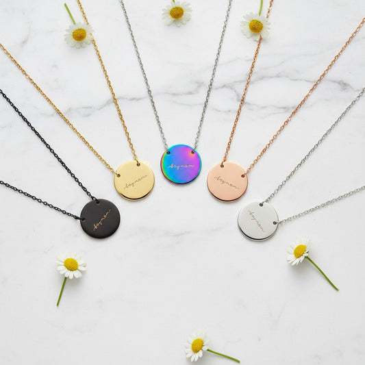 All five "Boy Mom" disc necklaces in black, gold, rainbow, rose gold, and silver arranged in a fan on white marble with daisies, complete necklace collection