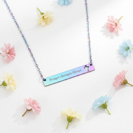 Engraved "Prayer Changes Things" bar necklace in rainbow iridescent with cut-out cross, flat lay on white marble with dried florals, colorful Christian jewelry gift