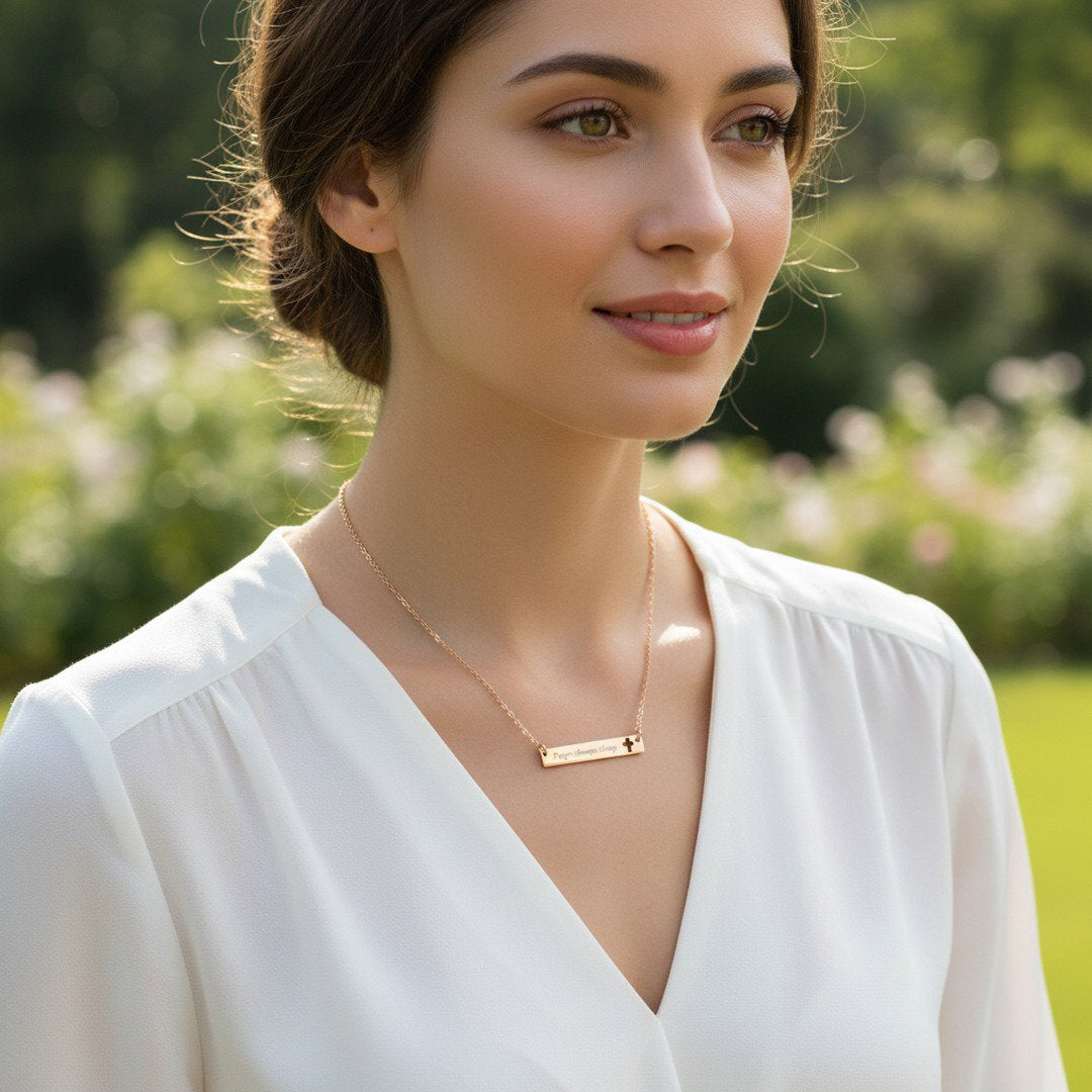 Close-up of rose gold "Prayer Changes Things" bar necklace with cut-out cross on blush linen with pink rose petals and pampas grass, faith gift for her