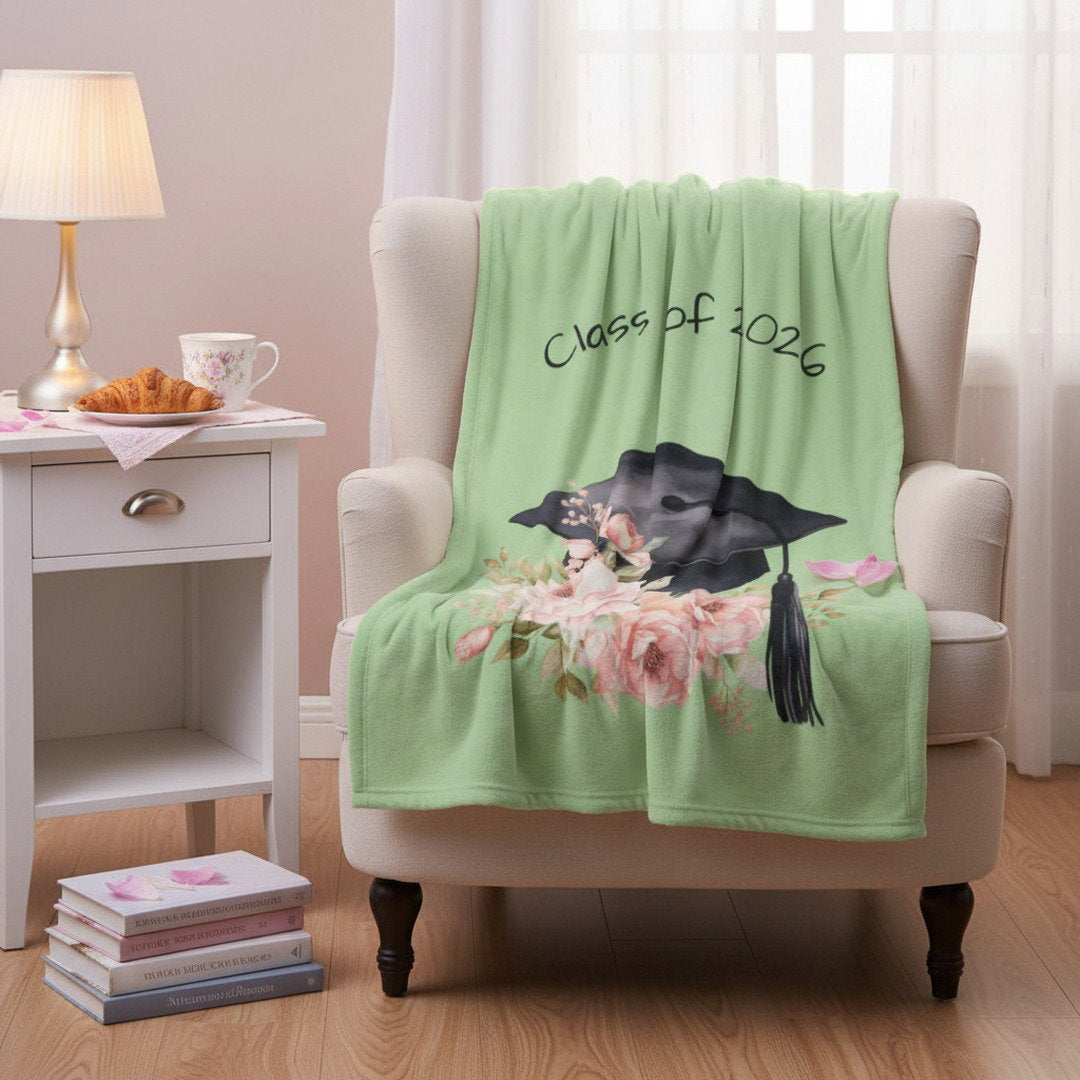 Sage green Class of 2026 graduation throw blanket with floral cap design draped over armchair, gift for girl grad