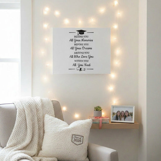 Graduation quote canvas on white wall surrounded by fairy lights above cozy chair with Class of 2026 pillow, sentimental dorm room wall art gift