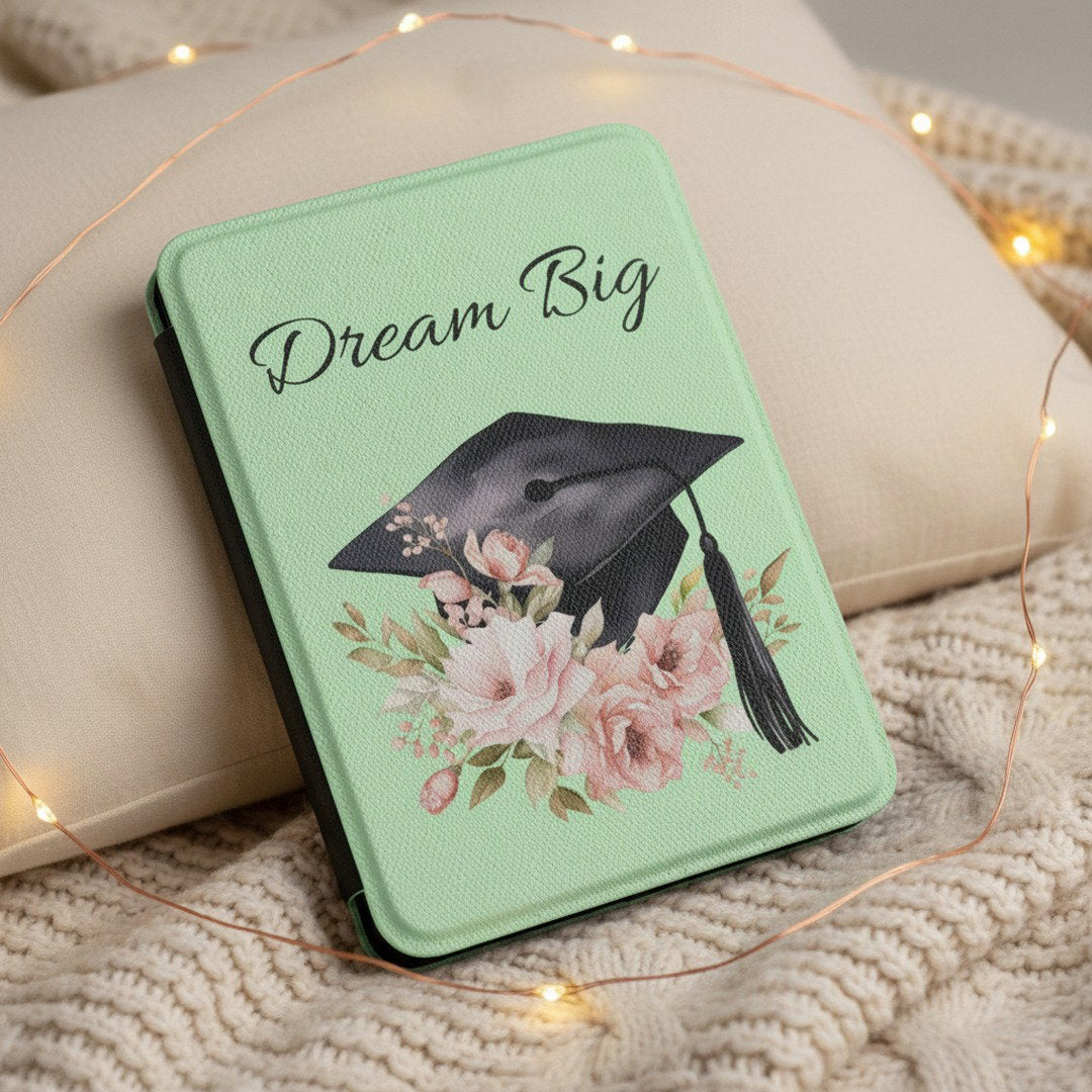 Mint green Dream Big Kindle case on cream knit blanket surrounded by warm fairy lights, cozy graduation gift for readers