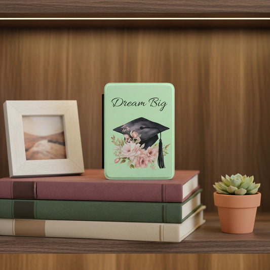  Dream Big graduation Kindle case standing on stack of books beside small photo frame and succulent, thoughtful graduation gift for book lovers