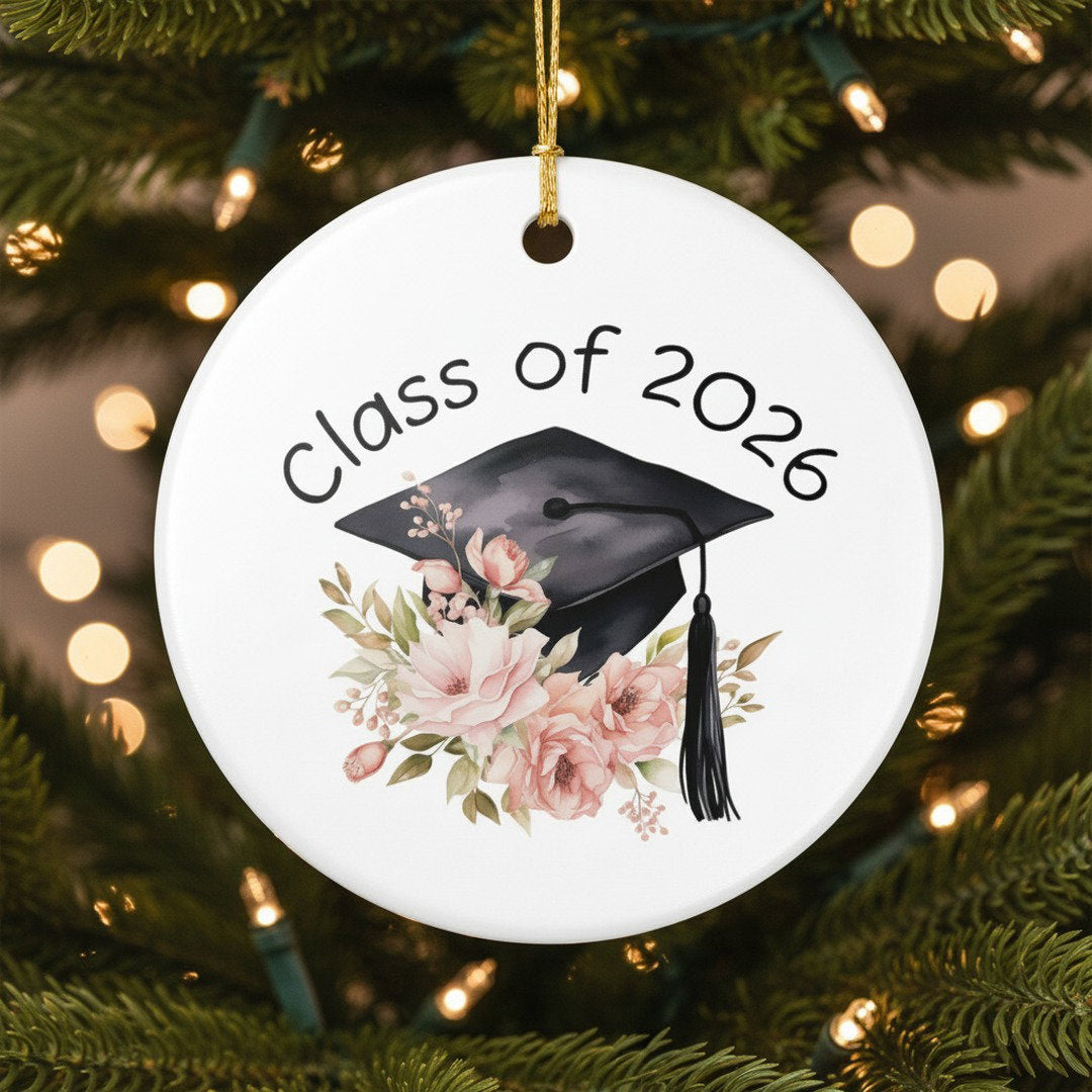 Class of 2026 floral ceramic graduation ornament hanging on lit Christmas tree, warm bokeh lights, meaningful grad keepsake gift