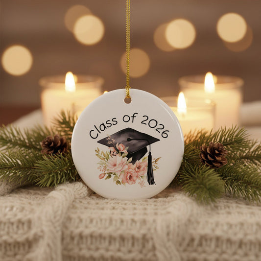 Class of 2026 floral graduation ornament displayed on cream knit blanket with pine branches and glowing candles, cozy holiday keepsake