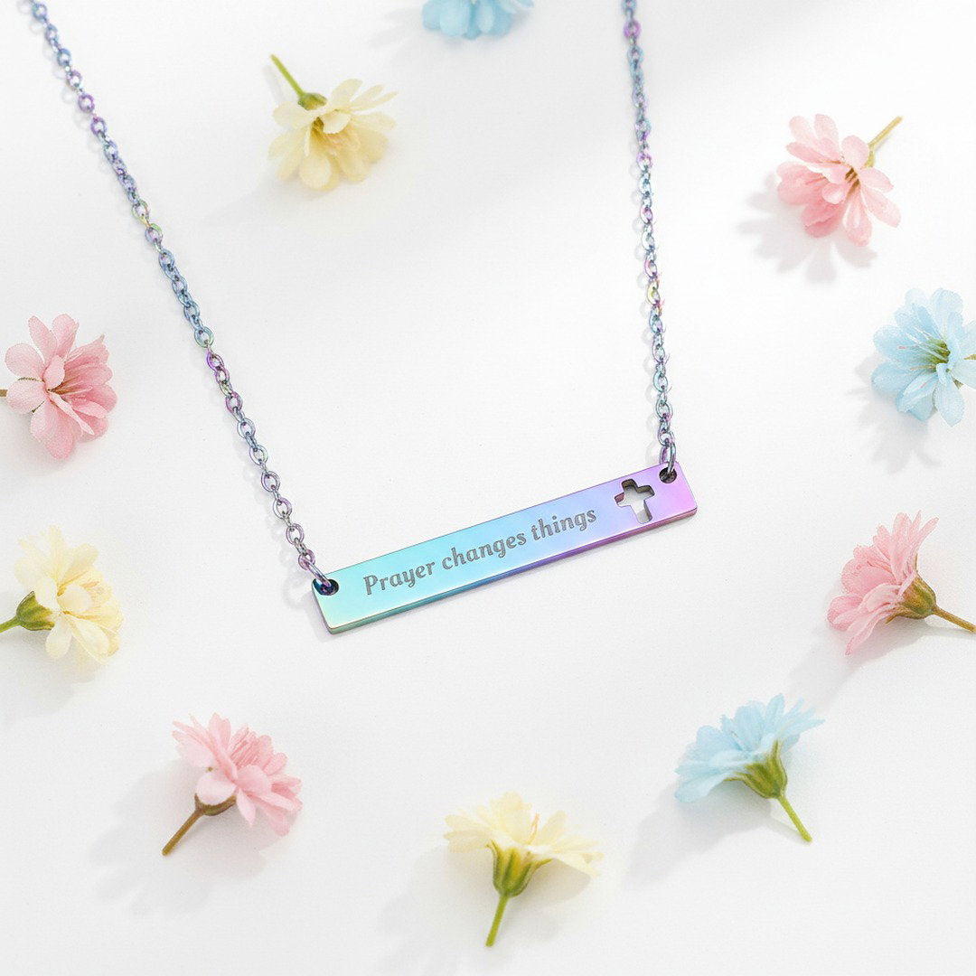Engraved "Prayer Changes Things" bar necklace in rainbow iridescent with cut-out cross, flat lay on white marble with dried florals, colorful Christian jewelry gift