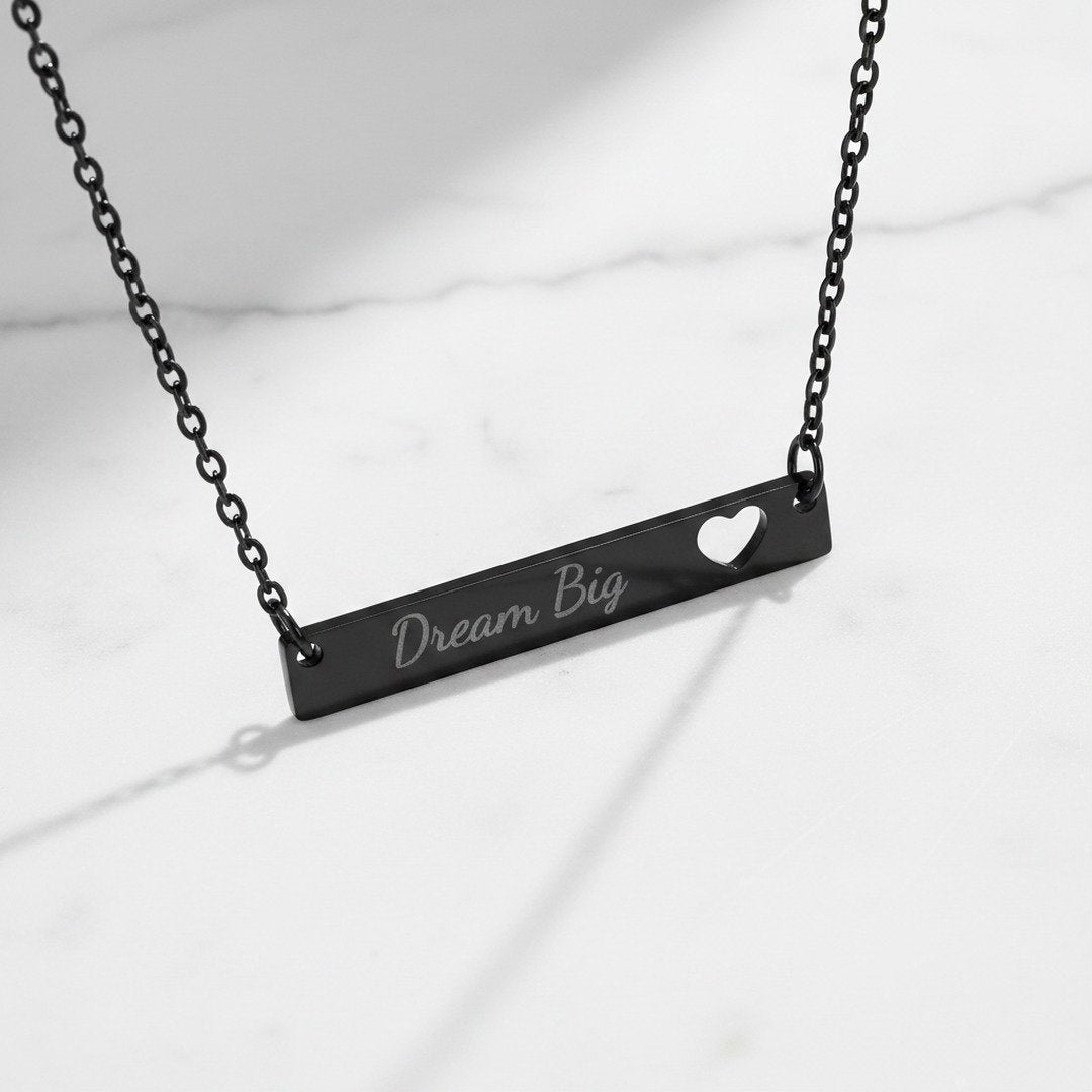 Black stainless steel Dream Big bar necklace with heart cutout on white marble surface