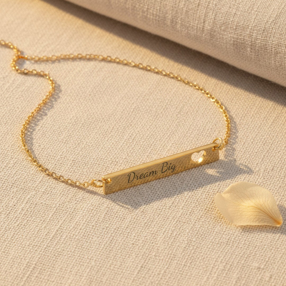 Dream Big engraved gold bar necklace with heart cutout on blush satin fabric