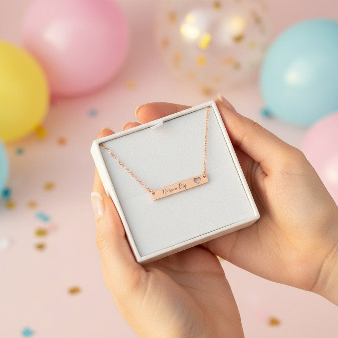 Rose gold Dream Big bar necklace in white gift box held by hands with colorful balloons in background