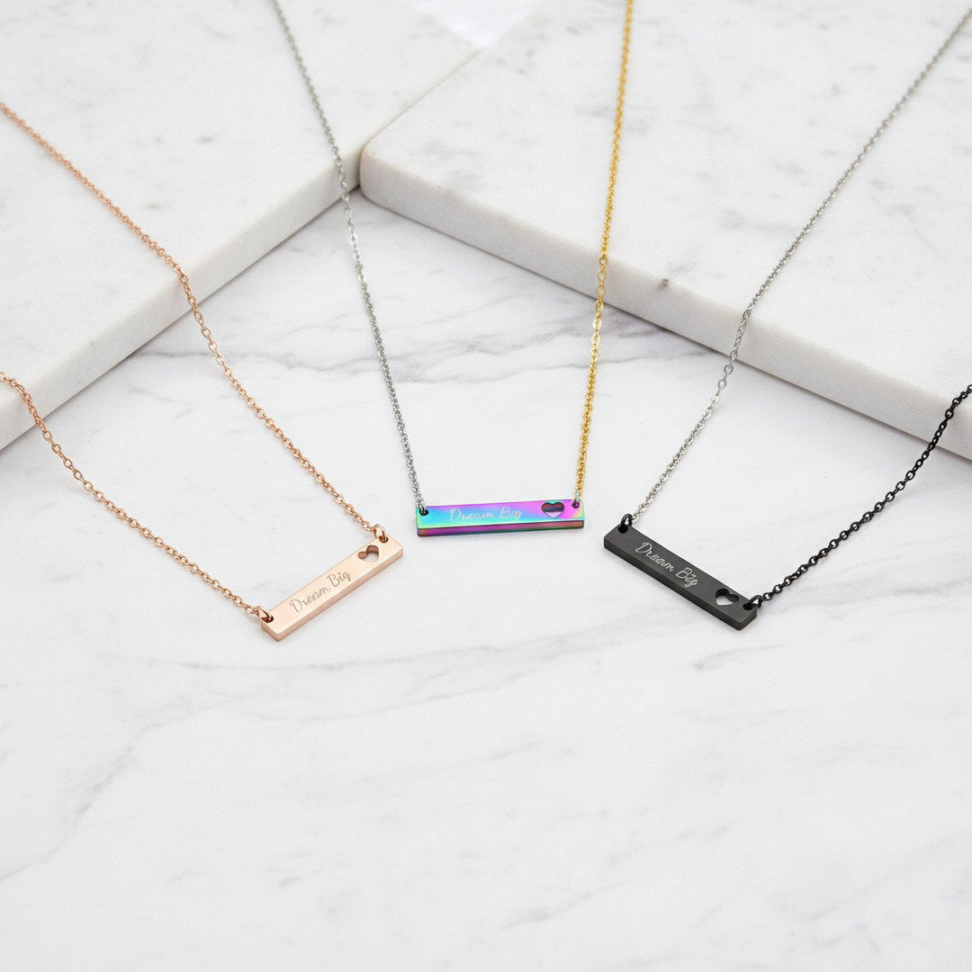 Dream Big bar necklaces in rainbow, gold, and black displayed on white marble surface