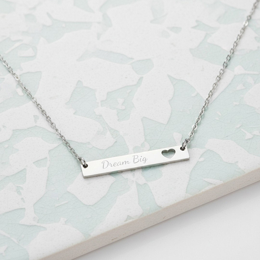 Silver Dream Big engraved bar necklace with heart cutout on light blue mosaic tile background