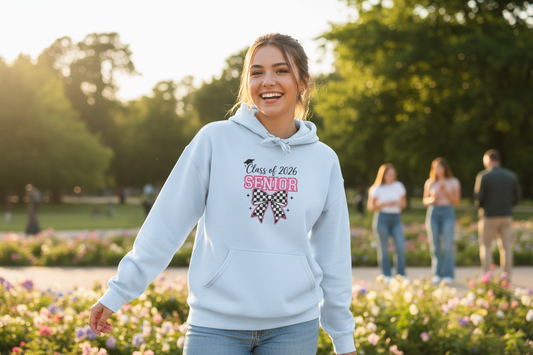 Young woman wearing a light blue Class of 2026 Senior Bow Hoodie smiling in a flower garden at golden hour, graduation celebration