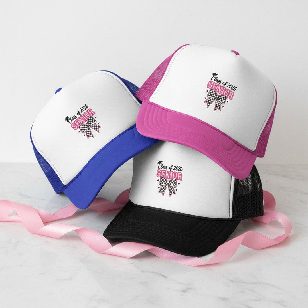 Class of 2026 Senior Bow trucker caps in pink, royal blue, and black stacked together on white marble with pink ribbon, checkerboard bow graduation cap gift for her