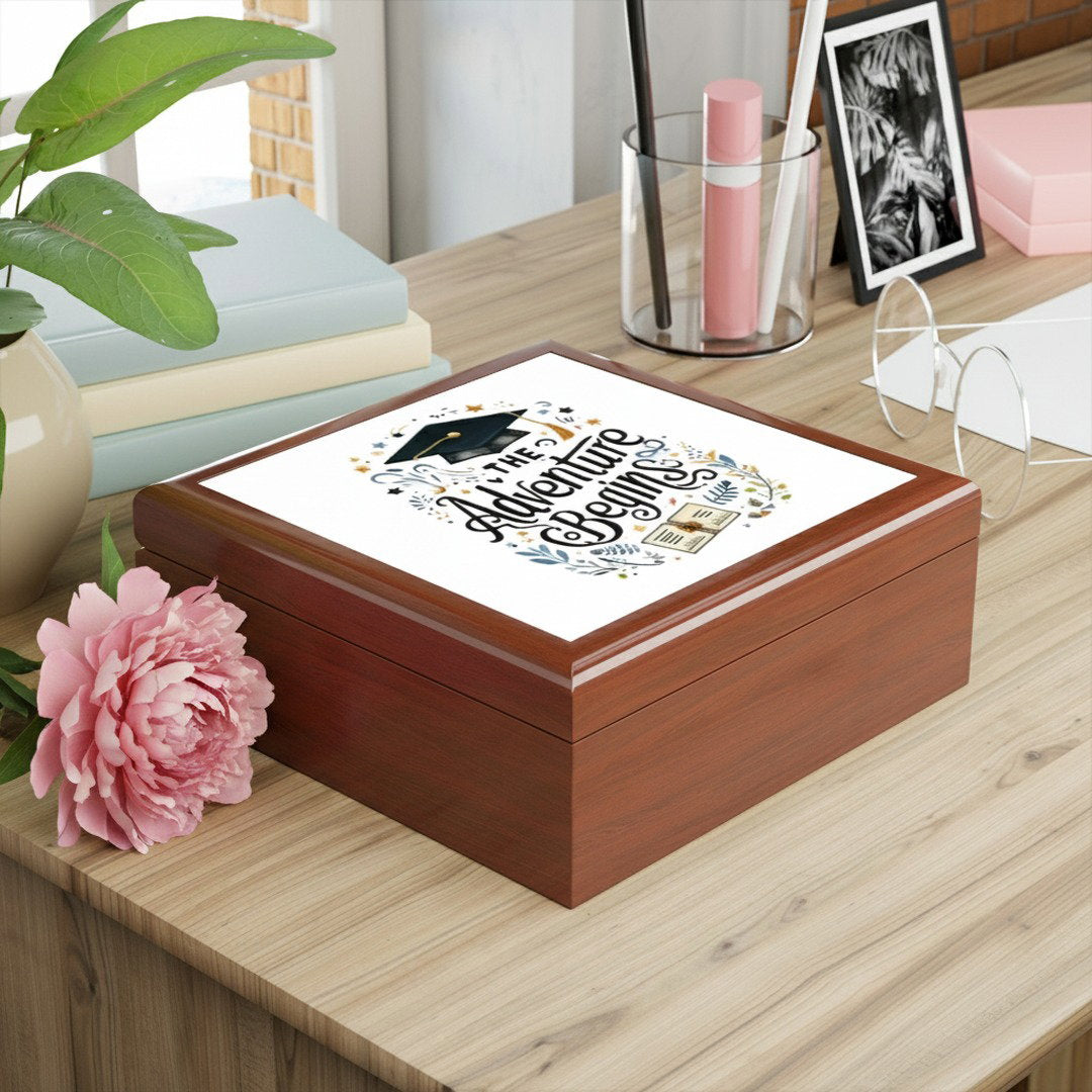 The Adventure Begins graduation jewelry box on a wood desk styled with a pink peony, books, and a framed photo