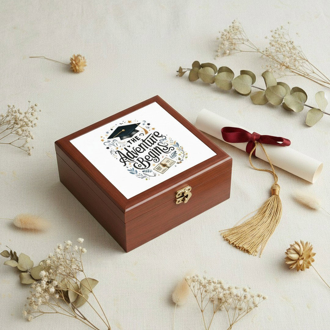 The Adventure Begins graduation jewelry box flat lay with dried eucalyptus, baby's breath, a diploma scroll, and gold tassel on a neutral linen surface