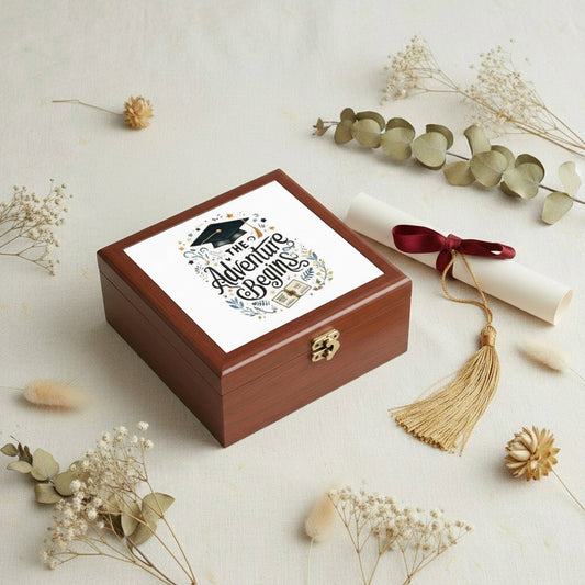 The Adventure Begins graduation jewelry box flat lay with dried eucalyptus, baby's breath, a diploma scroll, and gold tassel on a neutral linen surface