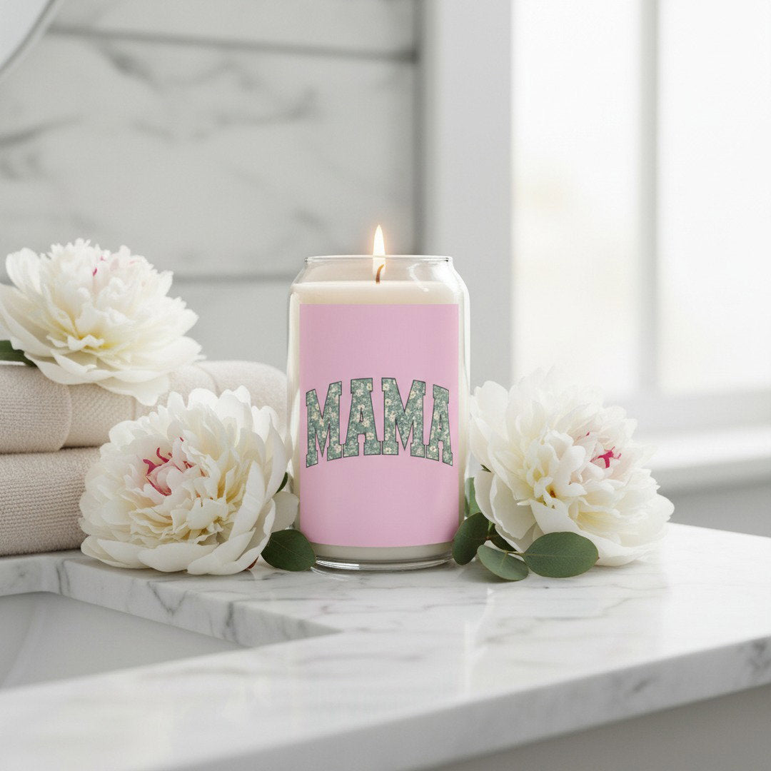 MAMA floral soy candle in glass jar with pink label, lit on white marble vanity surrounded by white peony flowers and folded towels, Mother's Day gift