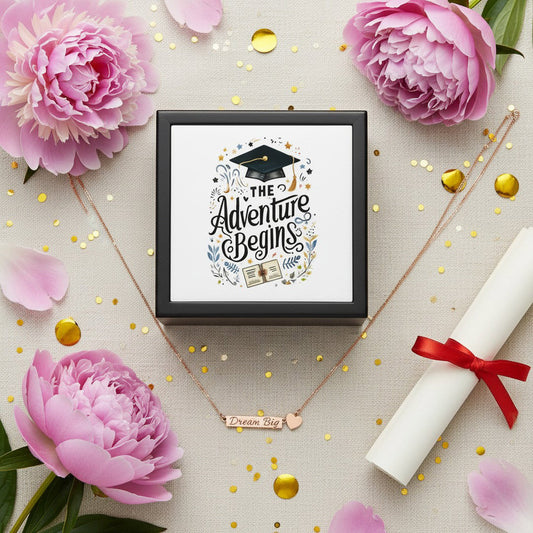 Adventure Begins graduation jewelry box with graduation cap lid design and rose gold Dream Big heart bar necklace arranged on cream linen with pink peonies, gold confetti, and diploma scroll, graduation gift bundle flat lay