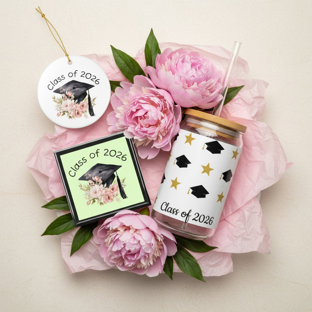 Class of 2026 graduation keepsake bundle with floral jewelry box, ceramic ornament, and gold star sipper glass arranged on cream background with pink peonies and pink tissue paper, overhead flat lay graduation gift set