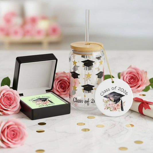  Class of 2026 graduation keepsake bundle with open floral jewelry box, ceramic ornament, and gold star sipper glass on white marble surface with pink roses, gold confetti, and diploma scroll, elegant graduation gift set display