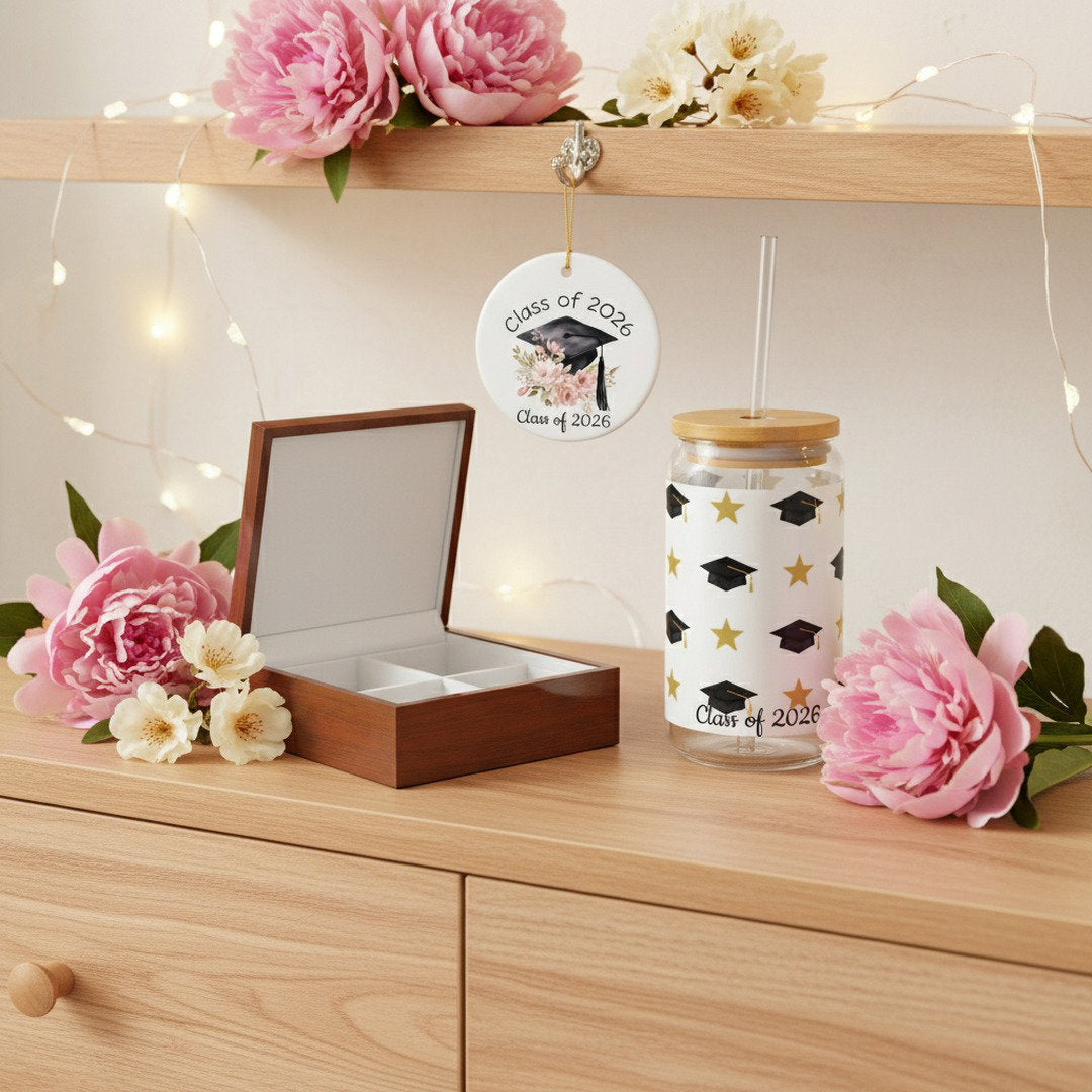 Class of 2026 graduation keepsake bundle with open wooden jewelry box, ceramic ornament hanging from shelf, and gold star sipper glass on light wood dresser with pink peonies, white flowers, and warm fairy lights, cozy graduation gift lifestyle photo