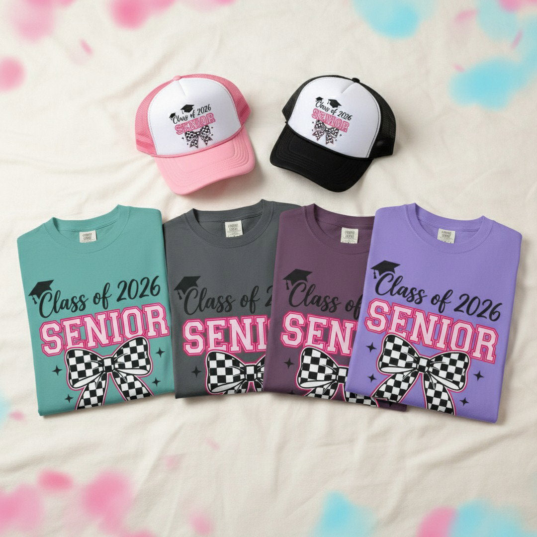  Four Class of 2026 Senior checkered bow t-shirts in seafoam, charcoal, dark berry, and violet folded in a row with pink and black Senior checkered bow trucker caps on white fabric with pink and blue confetti, graduation t-shirt and hat bundle color options